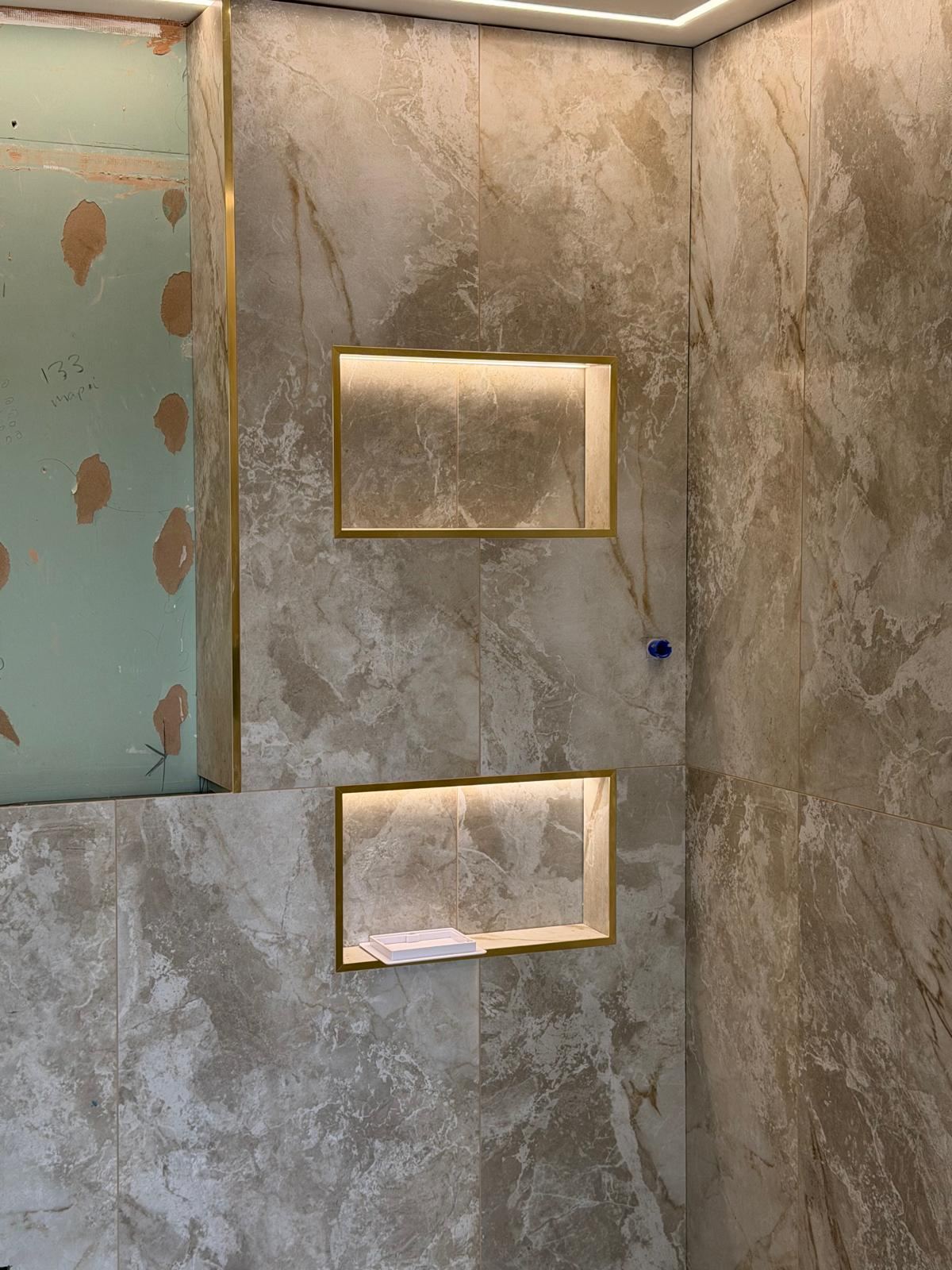 Backlit LED display niches with brass trim in a tiled bathroom