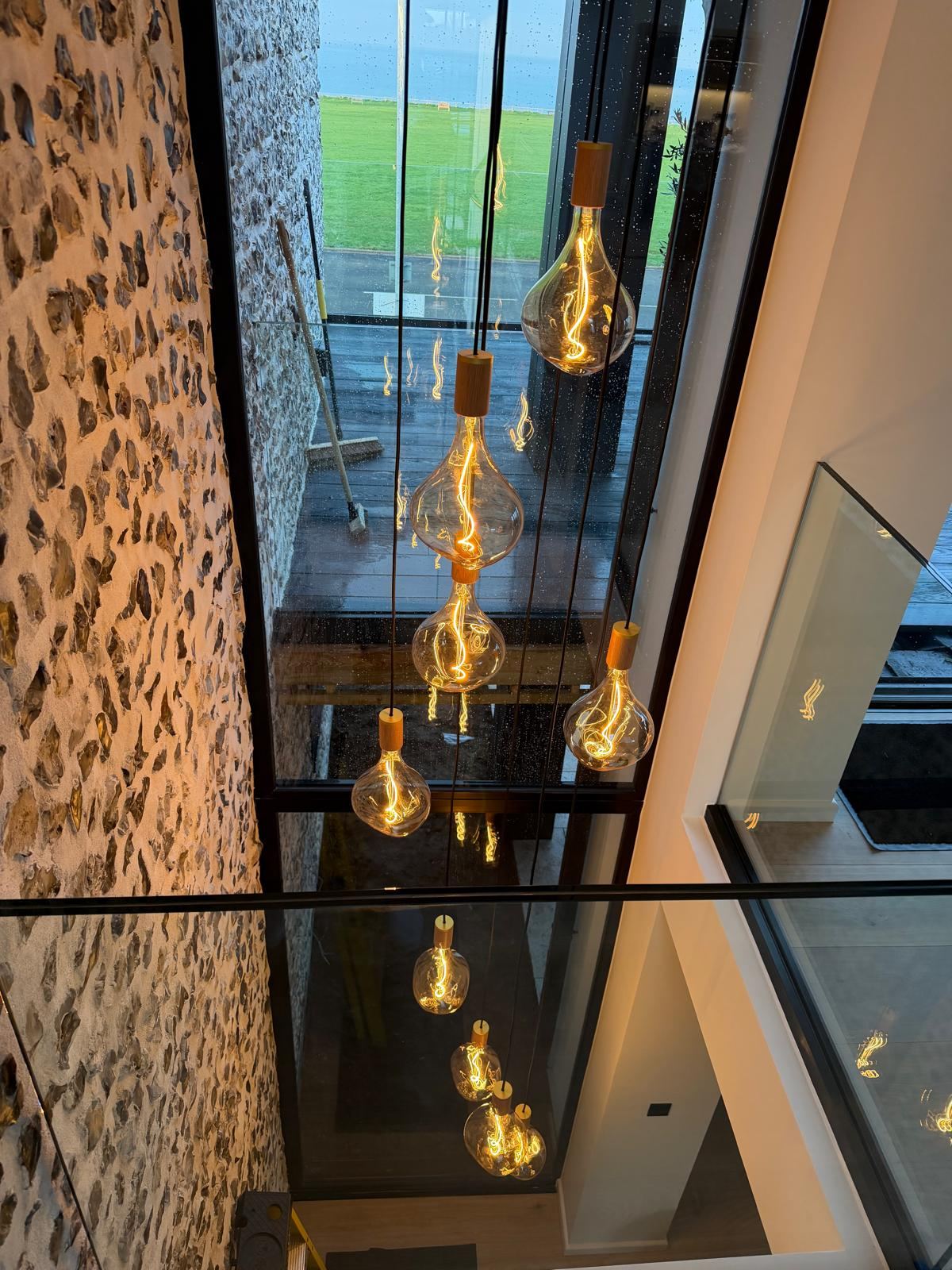A cluster of amber filament pendant bulbs hanging through a double-height stairwell