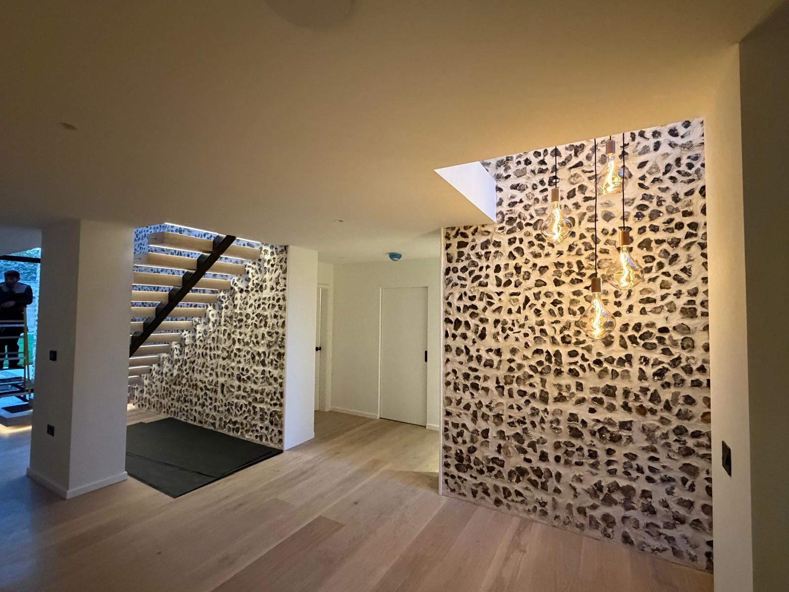 Entrance hall with integrated LED stair lighting and pendant bulbs against a flint wall